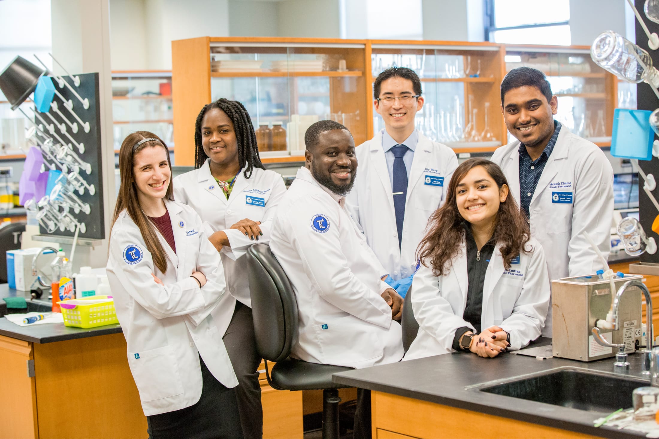 diverse group of students in white coats posing in lab